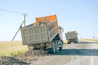 Yolda çakıllı bir çöp kamyonu. Çöp kamyonları yol kenarında çakıl taşı yığını oluşturuyor. Büyük bir inşaat kamyonu.
