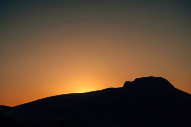 Güneş dağ siluetinin arkasında batıyor. Dağlık bir bölgede gün batımı.