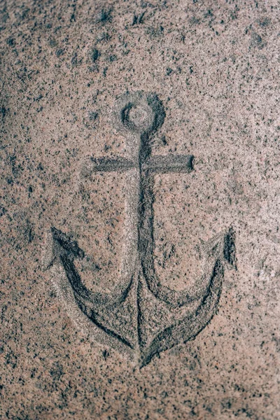 Sign of the sea anchor carved on the stone. Silhouette of a sea hook on granite. Stone engraving