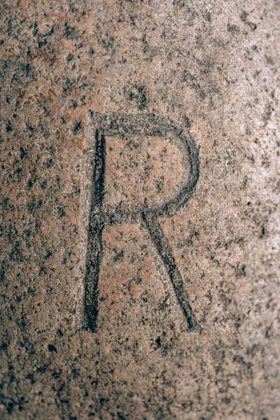 Letter R carved on the stone. Alphabet letter on granite. Stone engraving