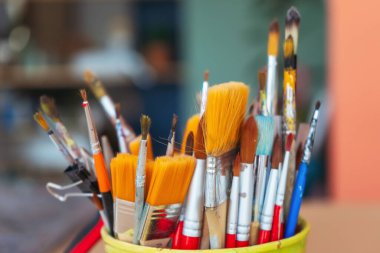 Atölyenin arka planında bir kavanozda yakın plan fırçalar. Ahşap saplı sanatsal fırça. Mobilya ve dekorları tebeşirle boyamak için atölyedeki masaüstü.