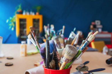 Atölyenin arka planında bir kavanozda yakın plan fırçalar. Ahşap saplı sanatsal fırça. Mobilya ve dekorları tebeşirle boyamak için atölyedeki masaüstü.