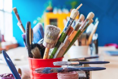 Atölyenin arka planında bir kavanozda yakın plan fırçalar. Ahşap saplı sanatsal fırça. Mobilya ve dekorları tebeşirle boyamak için atölyedeki masaüstü.