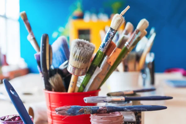 Atölyenin arka planında bir kavanozda yakın plan fırçalar. Ahşap saplı sanatsal fırça. Mobilya ve dekorları tebeşirle boyamak için atölyedeki masaüstü.