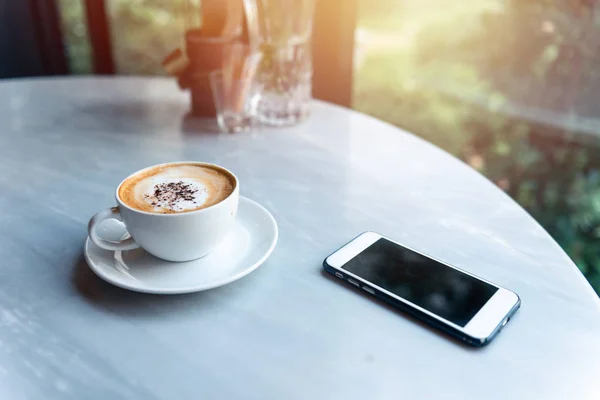 Kahve fincanı ve akıllı telefon güneş ışığı ile masada sabah