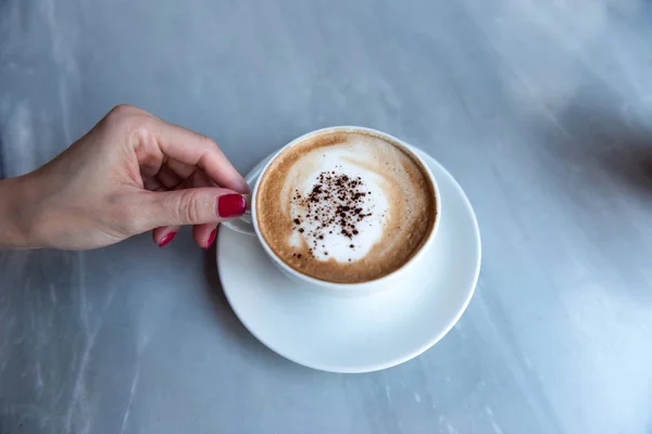 Kahve fincanı tutan kırmızı çivili kadın eli 