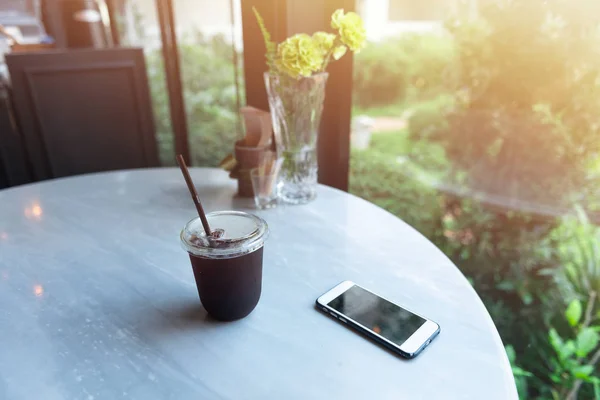Buz americano ve güneş ışığı sabah ile masada akıllı telefon
