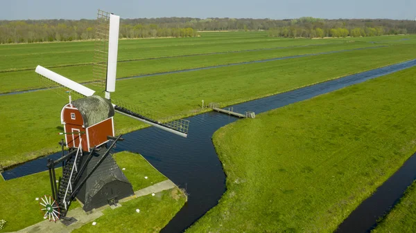 Légi felvétel egy régi holland hagyományos szélmalom a vidéki vidéken a hollandiai egy gát, csatornák. Vasúti. híd és egy út. — Stock Fotó