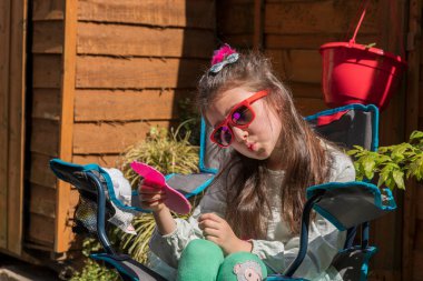 Üzgün yüzlü, elinde oyuncakla bahçede bankta oturan beyaz bir kız. Açık havada bir oyuncakla çocuk portresi..