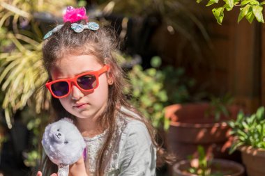 Üzgün yüzlü, elinde oyuncakla bahçede bankta oturan beyaz bir kız. Açık havada bir oyuncakla çocuk portresi..