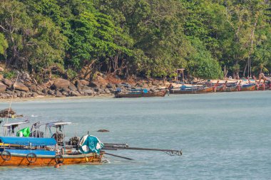 Kayalık bir adanın yakınındaki kristal berrak turkuaz sularda zarifçe gezinen bir teknenin huzurlu ve huzurlu görüntüsü.