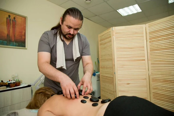 The masseur massages the woman with the help of heated stones. General plan