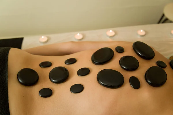 Massage parlour. On the body of a woman are heated stones for massage. Around the beautifully lit candles.