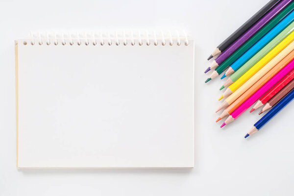 notepad with color pencil on white table view from above