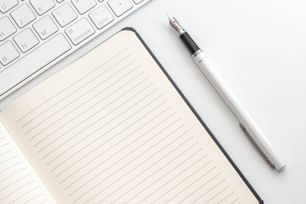 белый стол с блокнотом, клавиатурой и перьевой ручкой. Вид сверху
