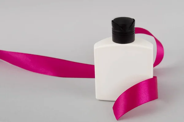 Белая бутылка с розовой лентой. Косметика тела. Подарок с лентой. Шампунь. Парикмахер — стоковое фото