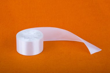 Şık beyaz saten kurdele. Turuncu zemin üzerine şerit. İpek beyaz şerit. Bir rulo bant. Dikiş Atölyesi