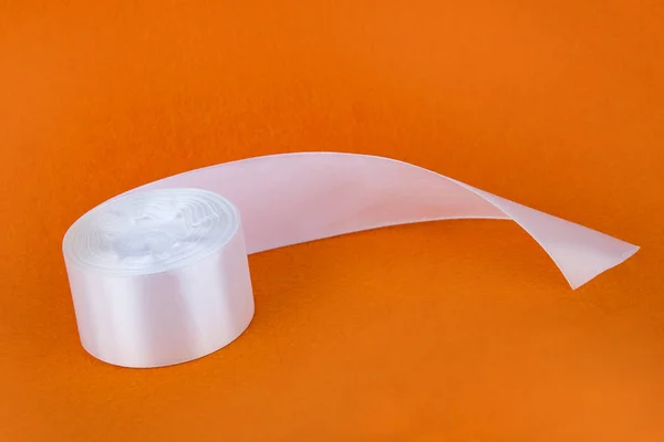 Şık beyaz saten kurdele. Turuncu zemin üzerine şerit. İpek beyaz şerit. Bir rulo bant. Dikiş Atölyesi