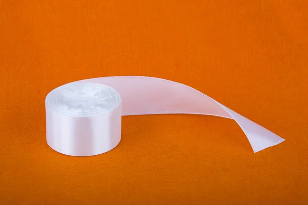 Şık beyaz saten kurdele. Turuncu zemin üzerine şerit. İpek beyaz şerit. Bir rulo bant. Dikiş Atölyesi