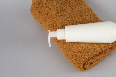 gri bir arka plan üzerinde kahverengi havlu ve duş jeli. yüz kremi ve havlu masanın üzerinde. Kozmetik Spa marka düzeni. Beyaz bir arka plan üzerinde katlanmış krem ve banyo havluları