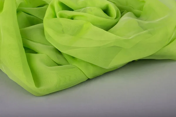 Green fabric on a gray background. Silk fabric. green background thin green fabric. silk textures in satin or velvet. Emerald or green silk background