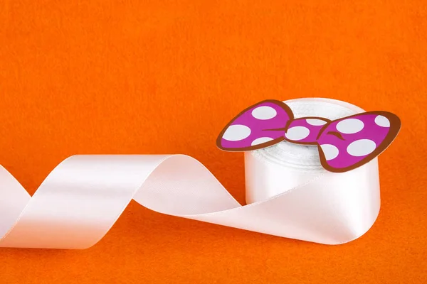 Turuncu arka planda beyaz şerit. Pembe kağıt yay. Beyaz saten kurdele. Bir rulo kaset. Dikiş atölyesi