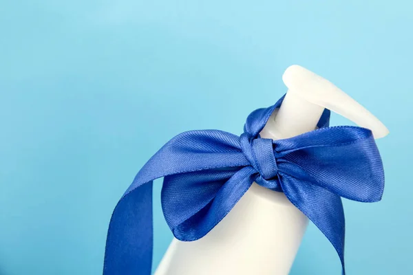 White bottle with blue ribbon on blue background. Gift with ribbon. body cream with a bow. facial skin care — Stock Photo, Image