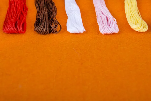 colored threads on an orange background. multicolored multicolored rainbow threads for embroidery close-up, accessories for sewing and embroidery in the sewing workshop