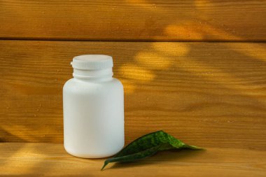Ahşap arka planda beyaz şişe. şişe ve yeşil yaprakları. Doğal kozmetik ürün. Masaj için yağ. Bitkisel şampuan