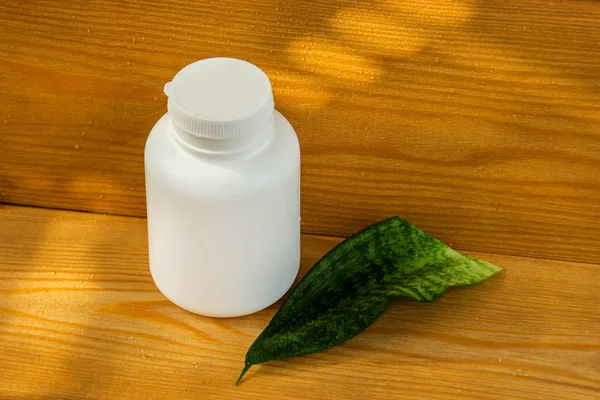 White bottle on wooden background. bottle and green leaves. Natural cosmetic product. Oil for massage. Herbal shampoo