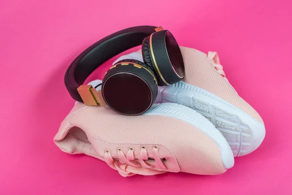kadın spor ayakkabıları ve kulaklıklar. Pembe arka planda pembe spor ayakkabılar. Yukarıdan görüntüleyin. Koşmak için müzik. Spor tarzı düz yatıyordu. Parlak arka planda kablosuz siyah kulaklıklar.