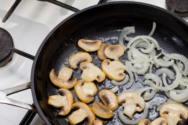 Fried sliced champignons with onions in a pan. Mushrooms with onions in a pan. Cooking lunch and dinner. Fried onion rings.