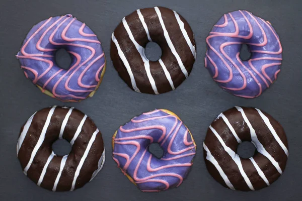 Donuts of violet and chocolate colored with striped pattern on dark background