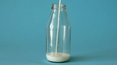 Taze çiftlik sütü mavi arka planda cam şişeye dökülüyor. Süt, cam şişenin tepesine dökülüyor, kapat. Plastiksiz