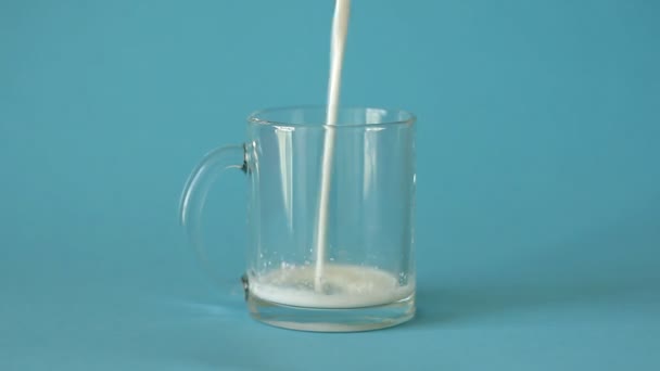 Frische Bauernmilch Ergießt Sich Gläserne Transparente Tasse Auf Blauem Hintergrund — Stockvideo