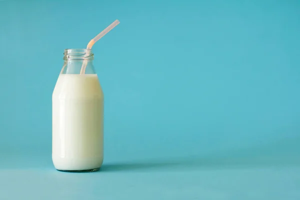 Fresh farm milk in glass bottle with pink color tubule on blue background front view. Milk in glass bottle to the top close up. Fresh farm milk is good for children's health and saturates the body with calcium and vitamin D