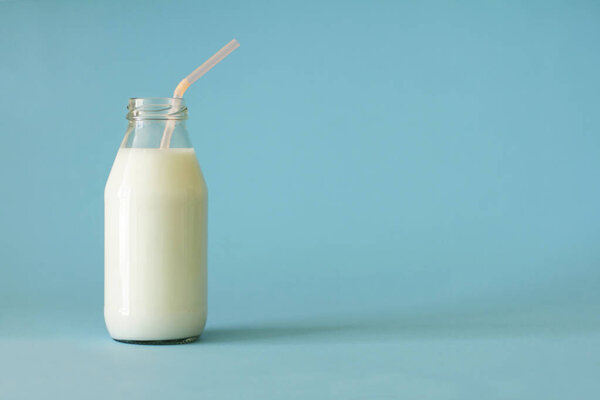 Молоко в стеклянной бутылке с тюбиками розового цвета на голубом фоне. Молоко в стеклянной бутылке до верха. Свежее фермерское молоко полезно для здоровья детей и насыщает организм кальцием и витамином D