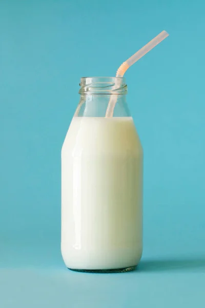 Fresh farm milk in glass bottle with pink color tubule on blue background close up front view. Milk in glass bottle to the top. Milk is good for children\'s health and saturates body with calcium and vitamin D