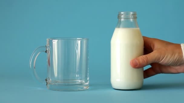 Main féminine prend bouteille de lait et verse le lait dans une tasse en verre sur fond bleu, vue de face. Plastique libre. Le lait frais de ferme est bon pour la santé des enfants et saturé le corps de calcium et de vitamine D