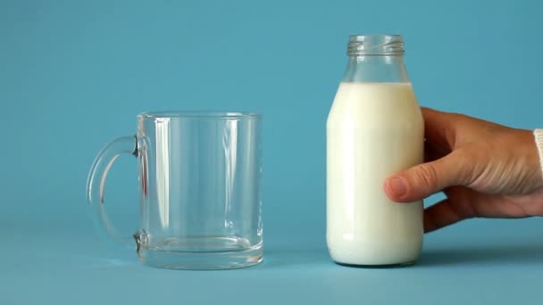 女性の手は牛乳のボトルを取り 青い背景 フロントビューにガラスカップに牛乳を注ぎます プラスチックフリー 新鮮な牛乳は子供の健康のために良いとカルシウムとビタミンDで体を飽和させます — ストック動画