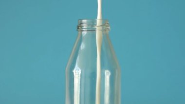 Taze çiftlik sütü mavi arka planda cam şişeye dökülüyor. Yakın çekim sütü mavi arka plan manzarasında cam şişeye dökülüyor. Kapat.