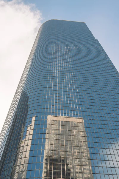 A tall glass sky scraper with reflections and blue sky