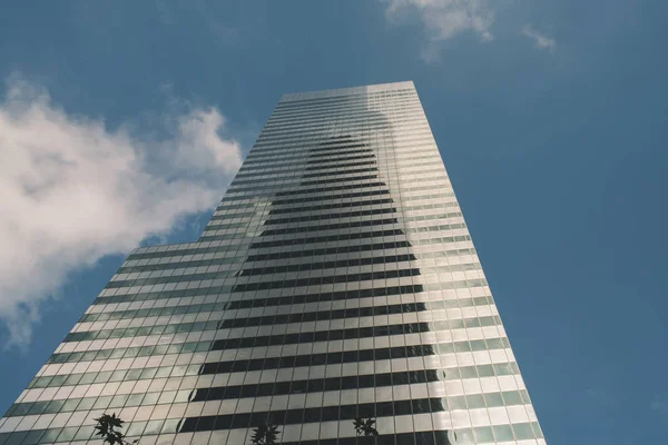A glass sky scraper leading up to the blue sky with white clouds