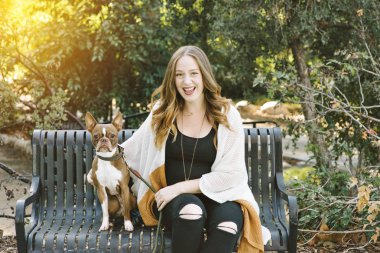 Beyaz kadın köpeğini yanında çok mutlu onun arkasında güneş ayarıyla bir bankta oturur