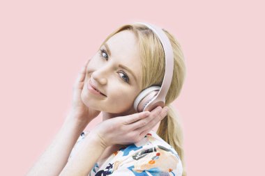 Genç bir beyaz kız kulaklıktan ve pembe bir arka plan üzerinde müzik dinleme önden görünümü
