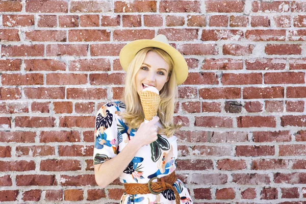 Hip young female with a fedora hat licks an ice cream on a hot day