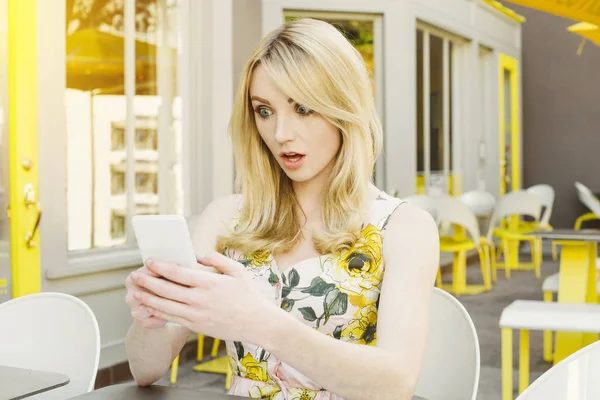 Pretty woman is shocked at photo or text that is on her smart phone at an outdoor cafe