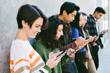 Bir grup genç yetişkin, şehirde bir duvarın önünde dururken cep telefonlarına bakıyor - Millennial - Teknoloji