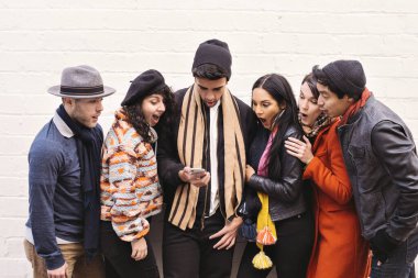 Genç arkadaşlar akıllı bir telefon ekranına bakar ve şaşırırlar - Urban - Winter - Sıcak kıyafetler