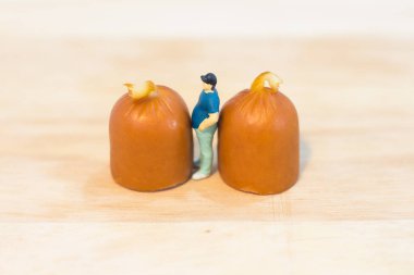 Minyatür insanlar: Şişman adamı kapatın ve beyaz arka planda izole edilmiş sosislere bakın (Gıda kavramı)